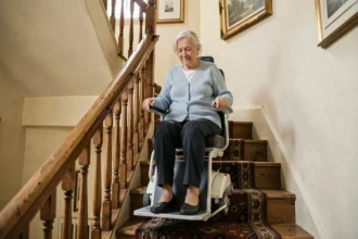 Femme âgée assise sur un monte-escalier portable installé dans un escalier en bois d'une maison française, tenant les accoudoirs avec une expression sereine